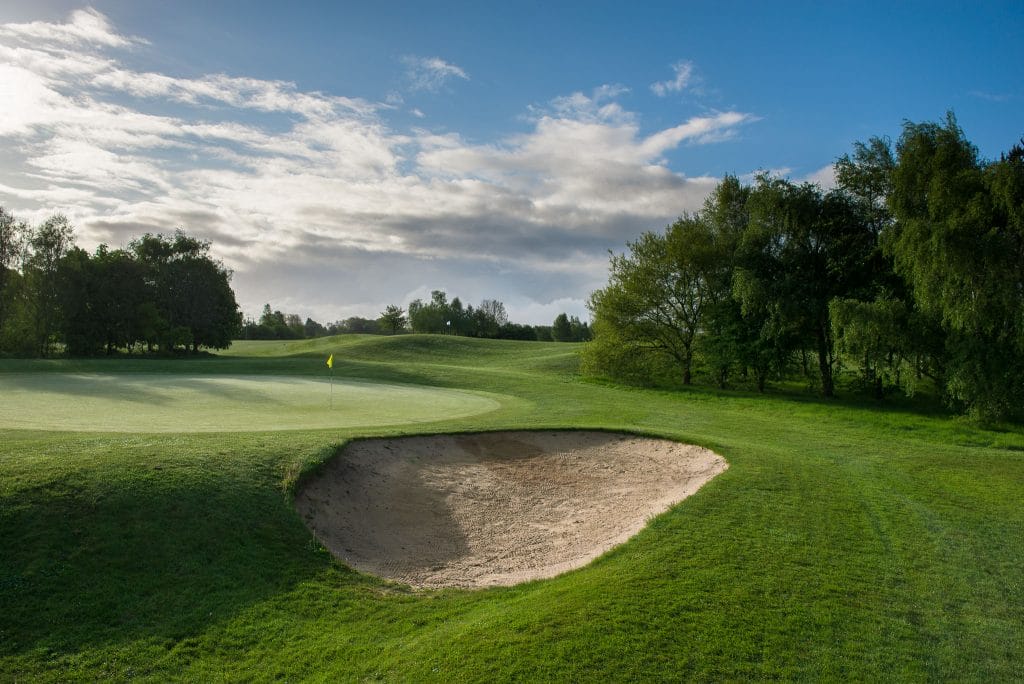 A quiet golf course under a dark, moody sky, with deep shadows over the fairway and trees silhouetted against the fading light, creating a dramatic and peaceful atmosphere.