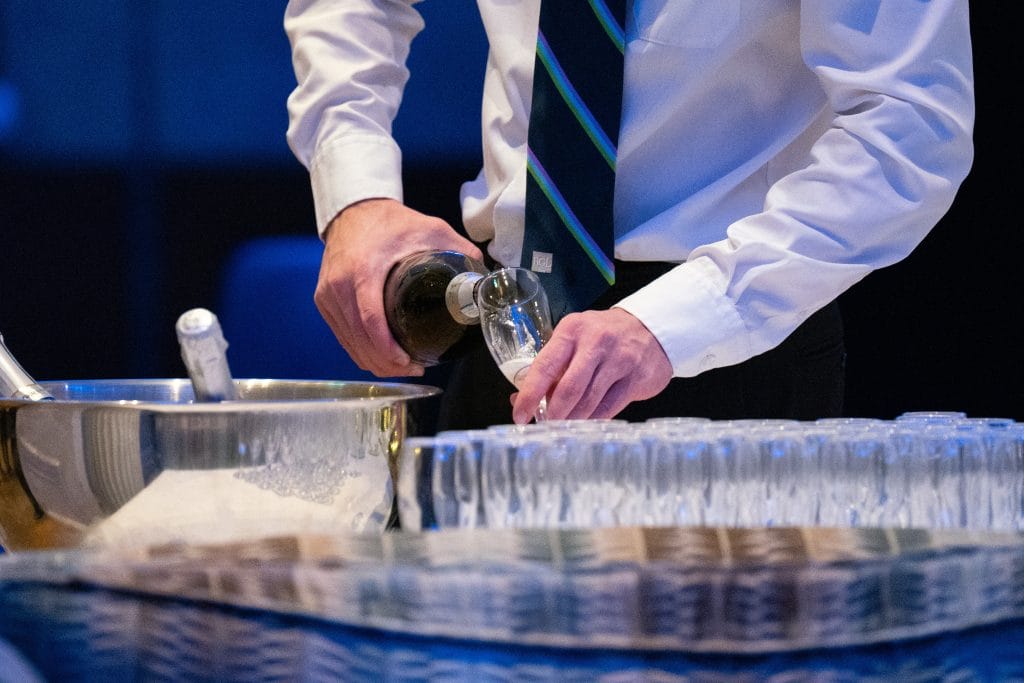 man in suit pouring champagne in glasses at a wake venue near bristol