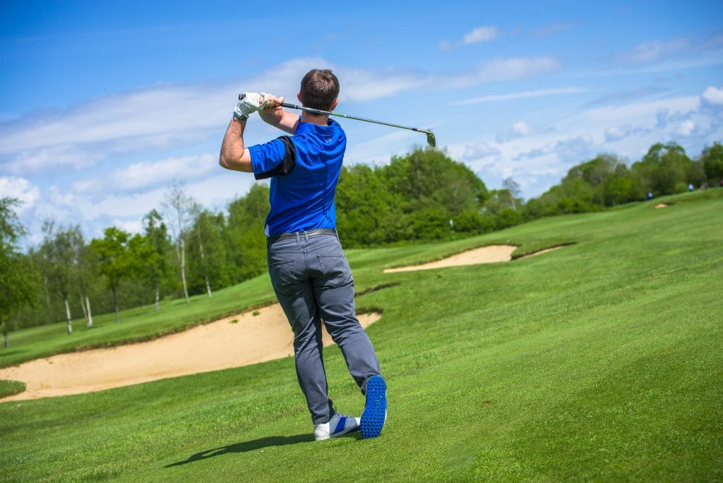 male golfer hitting ball towards green