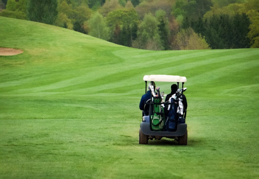 Two men driving a golf buggy across the fairway at a golf club in Bristol, enjoying golf days and using the driving range and golf shop facilities.